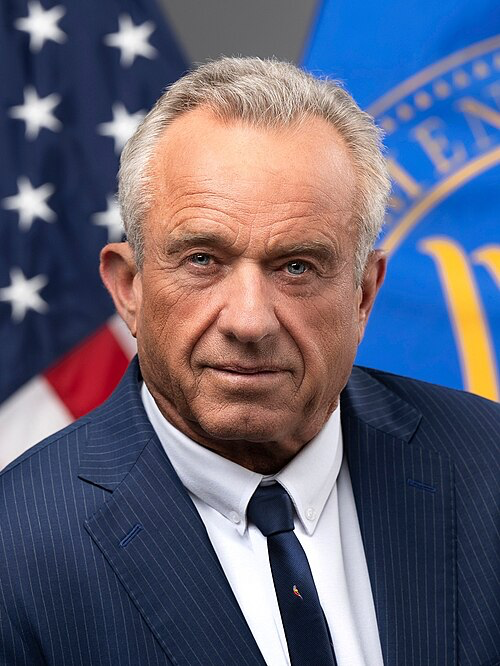 Official portrait of Robert F. Kennedy Jr. wearing a navy pinstriped suit and dark tie, positioned in front of an American flag and what appears to be a government seal.
