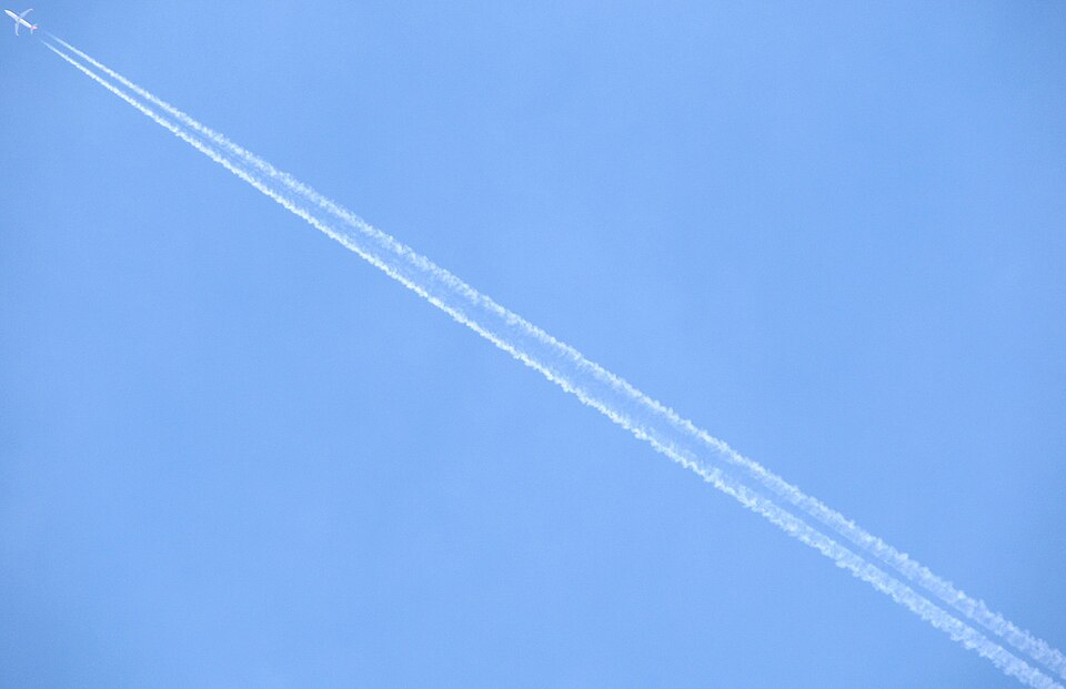 A bright blue sky with white chemtrails crossing diagonally from the upper left corner. These controversial aerial phenomena, which some claim contain harmful chemicals rather than being simple jet engine condensation, create a striking contrast against the deep blue background.