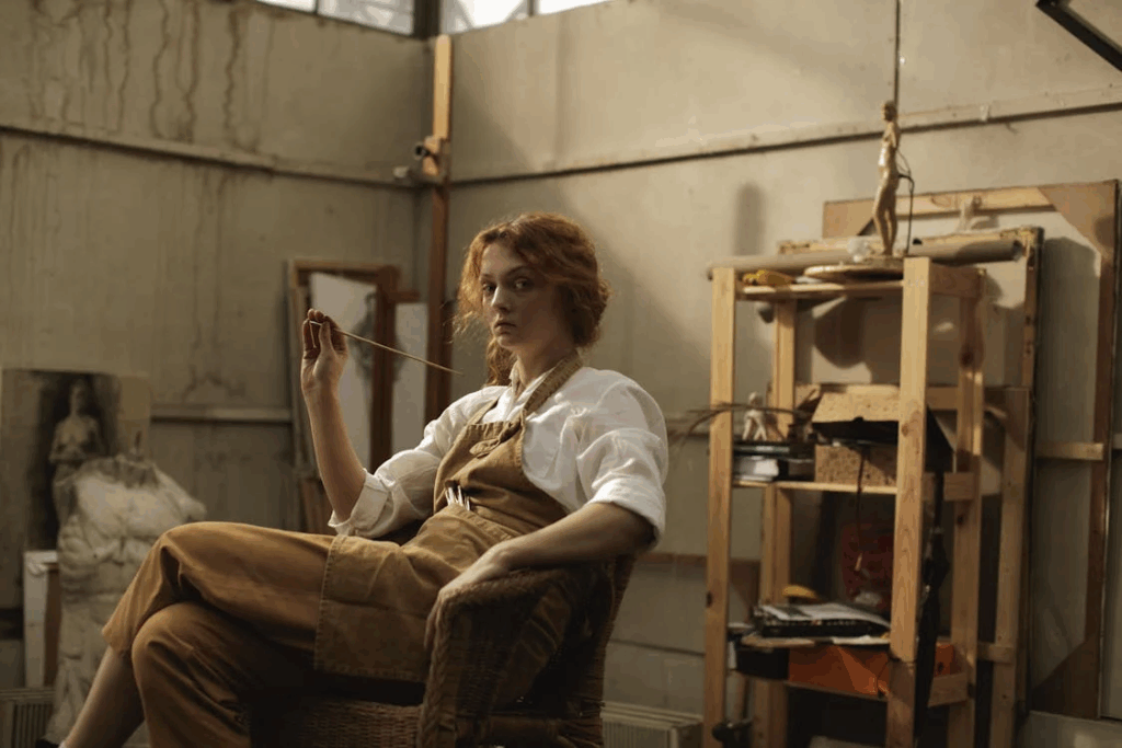 Woman in artist's studio sitting with thread in hand, demonstrating how seated posture can create psychological boundaries and signal self-protection in various environments.