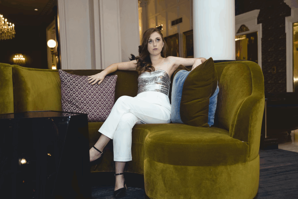 Woman in elegant attire on a green velvet couch with relaxed posture, showcasing how leg positioning communicates confidence and comfort in social settings.