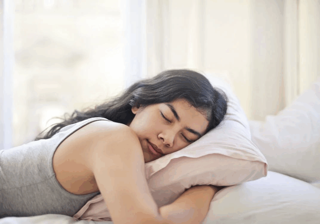 Woman sleeping peacefully in white bedding showing improved sleep quality during first week of liver recovery after drinking.