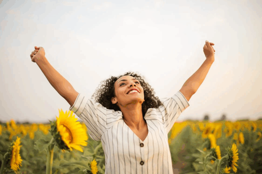 Happy woman with arms raised in sunflower field celebrating improved energy and wellbeing after two weeks without alcohol.