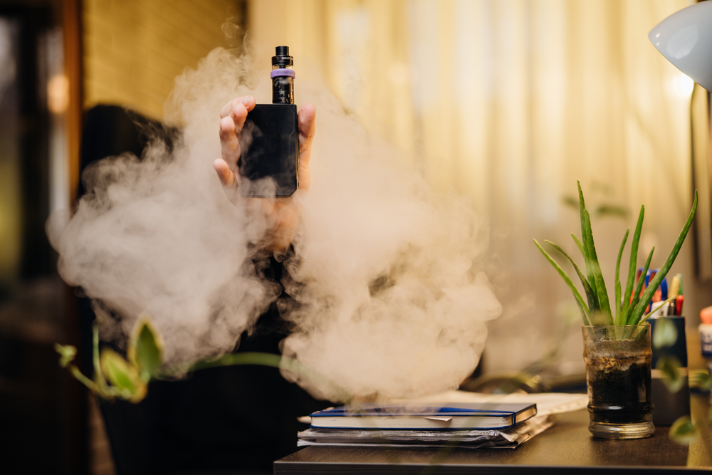 Exhaling the vapor with electronic cigarette.Puffing clouds of smoke.Vape flavor liquid chemicals.Use of e-cigarettes in the home.Smoking and vaping negative health effects.Nicotine addiction habit
