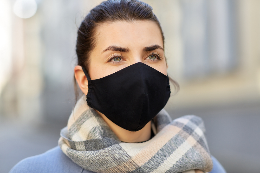 health, safety and pandemic concept - young woman wearing black face protective reusable barrier mask outdoors
