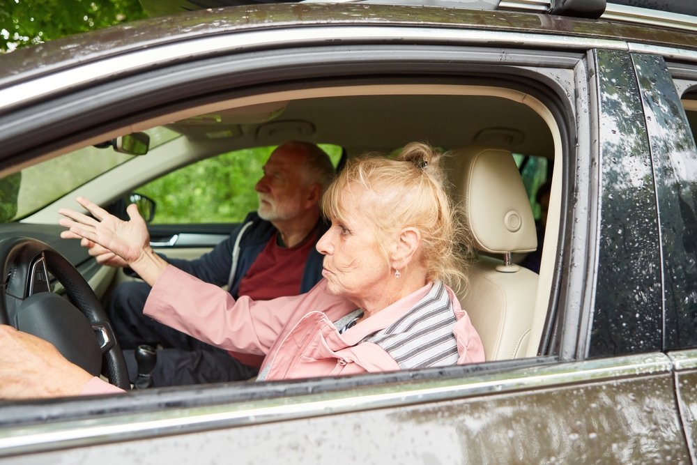 Furious elderly woman and man gesturing while traveling in car during road trip