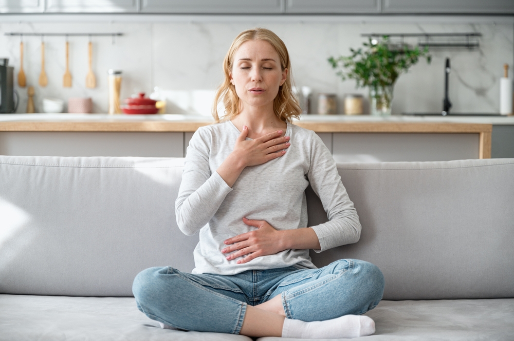 Concept of mental health. Woman sitting on couch and doing calming breathing exercises after panic attack. Female inhaling and exhaling to deep breath. Self-control, anxiety relief concept
