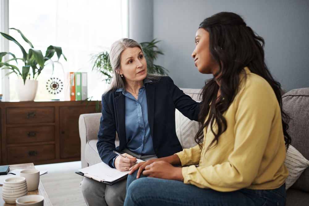 Woman, therapy and notes in office for mental health, talking with empathy or encouragement. Female therapist, patient and consulting room with discussion for stress and anxiety, support and help
