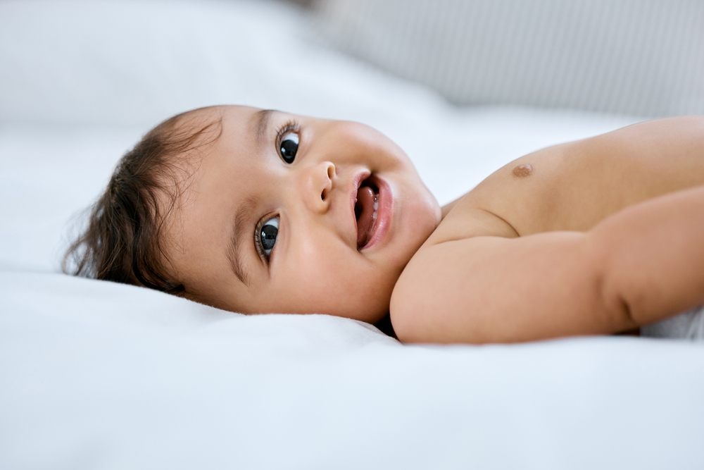 Baby portrait, smile and lying on bed for relax with healthy growth, cute and wellness in home. Infant girl, happy face and rest on mattress for development, youth and diaper change in bedroom
