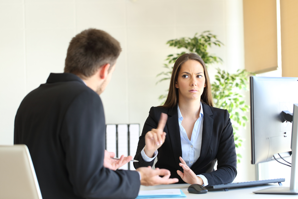 Boss denying something saying no with a finger gesture to an upset employee in her office
