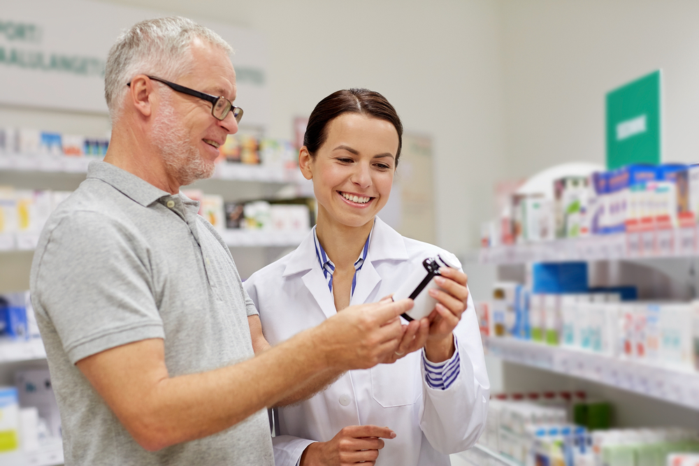 medicine, pharmaceutics, health care and people concept - happy pharmacist showing drug to senior man customer at drugstore