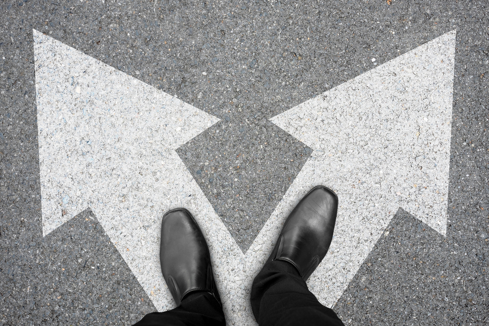 Businessman in black shoes standing at the crossroad making decision which way to go. Decision making concept.
