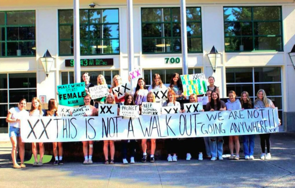 High school students holding protest banner reading 'XX This is not a walk out - We are not going anywhere' in front of school building.