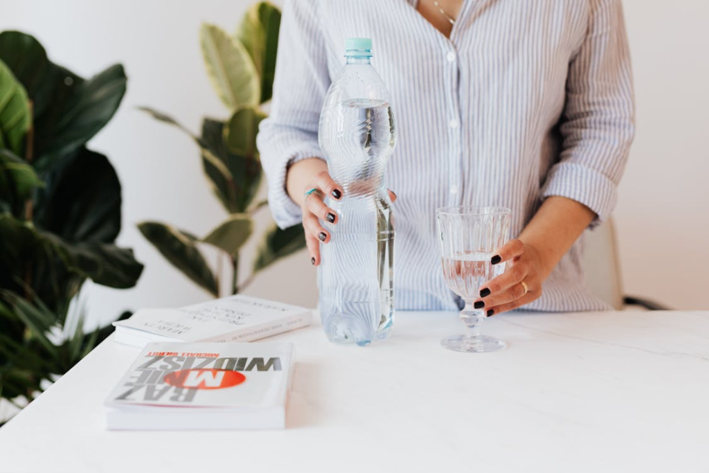 Crop woman with glass and bottle of water
