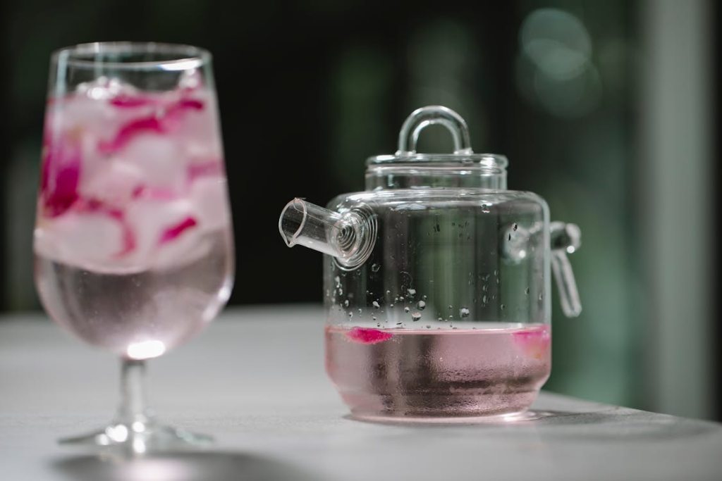 Glass and pot with cold water with rose petals

