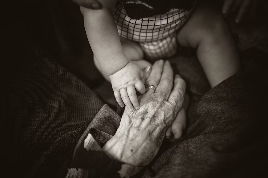 eldery hand handing a babies leg.