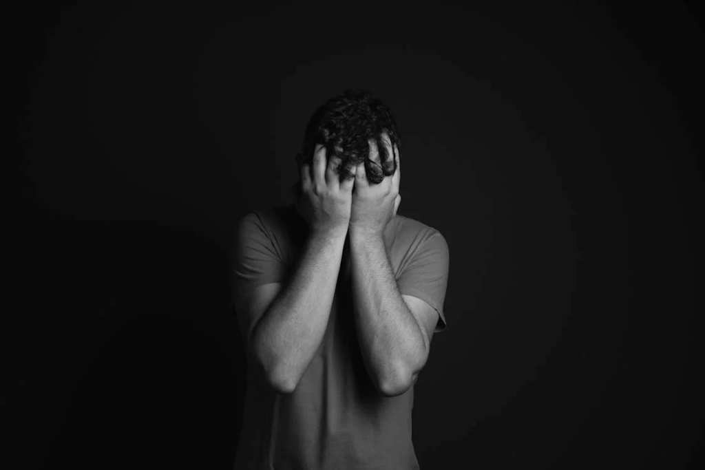 Person in dark room holding head in hands showing distress, illustrating how hoarding often accompanies depression and serves as a coping mechanism