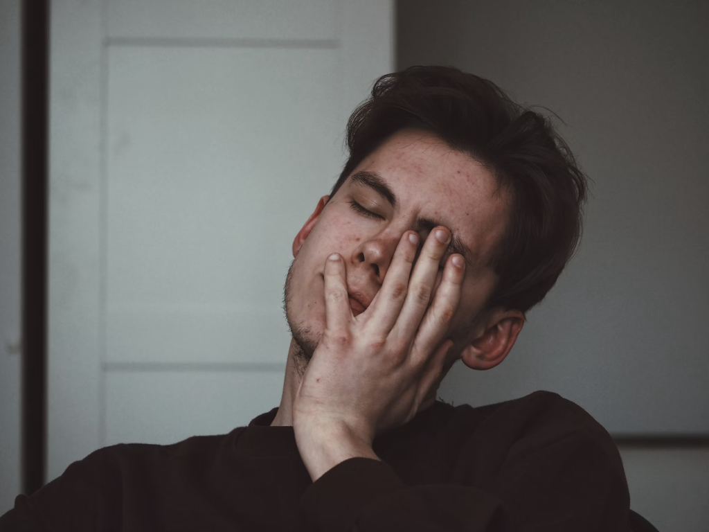 Tired man covering his face with his hand, demonstrating cancer fatigue symptom that doesn't respond to rest.