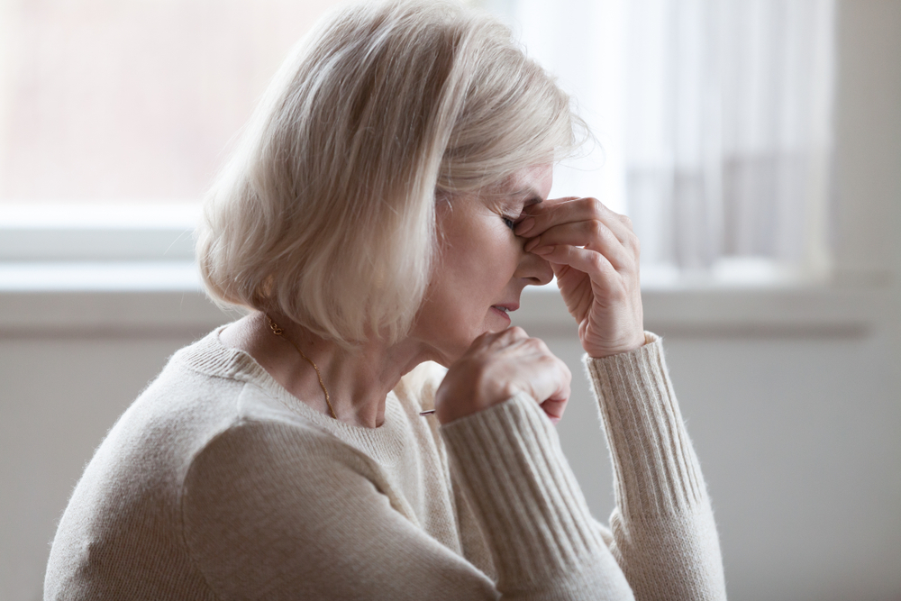 Fatigued upset middle aged older woman massaging nose bridge feeling eye strain or headache trying to relieve pain, sad senior mature lady exhausted depressed weary dizzy tired thinking of problems
