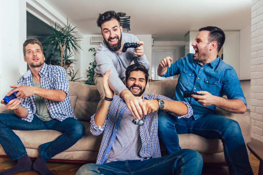 Smiling male friends playing video games at home and having fun.
