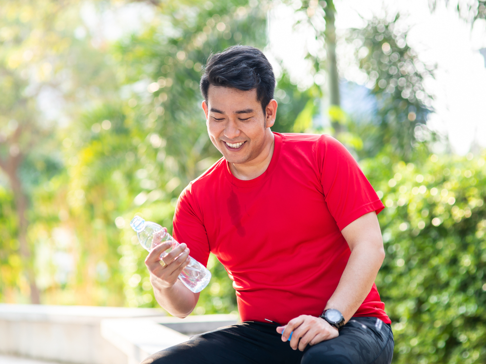 Asain sport man booking a bottle of water in his hand the park outdoor.
