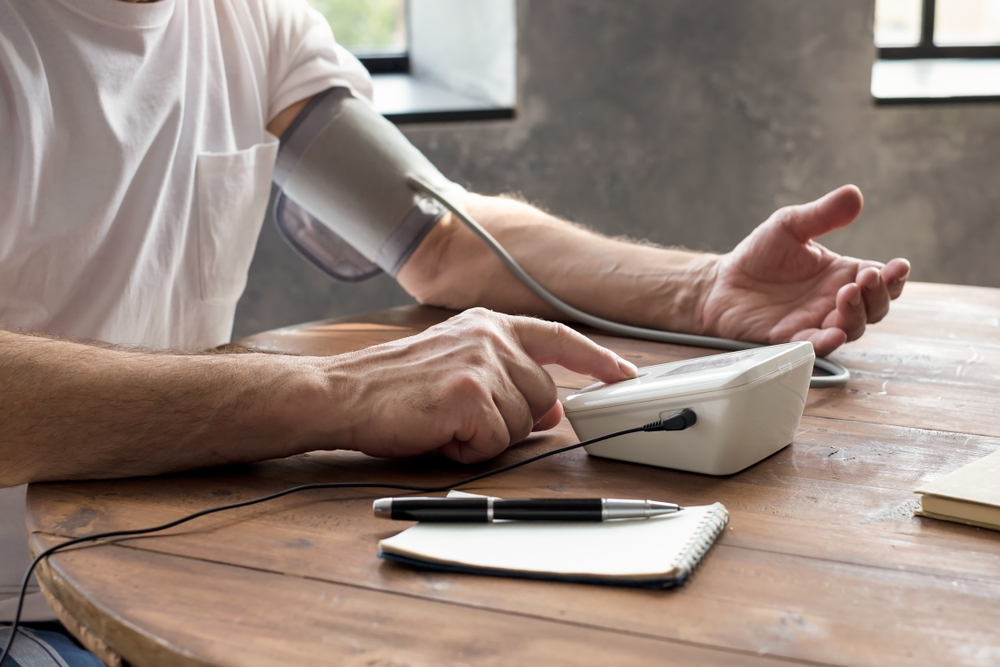 Senior man using a home blood pressure machine to check his health sitting at living room
