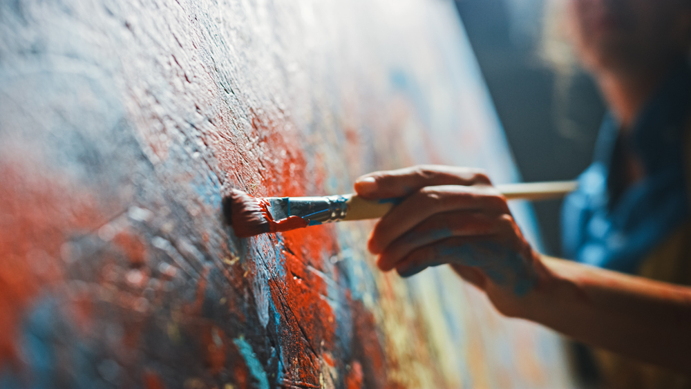 Female Artist Works on Abstract Oil Painting, Moving Paint Brush Energetically She Creates Modern Masterpiece. Dark Creative Studio where Large Canvas Stands on Easel Illuminated. Low Angle Close-up
