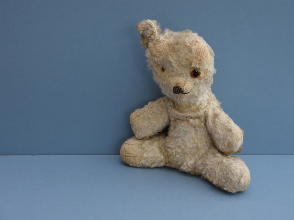Vintage Teddy bear in lovable play worn condition with missing eye, missing ear and missing fur. With blue background and space to left for caption. Childhood memories.