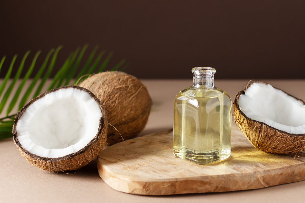 Bottle of coconut oil and fresh coconuts with palm leaf on wooden board over brown background. Coconut natural cosmetics.
