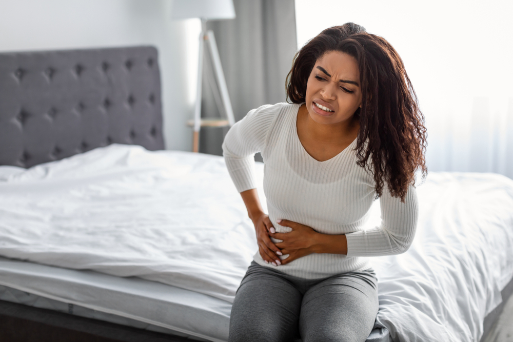 People, Healthcare and Health Problem Concept. Portrait of upset sick young black woman suffering from acute pain in right side, sitting on bed at home, free copy space. Abdomen liver pain
