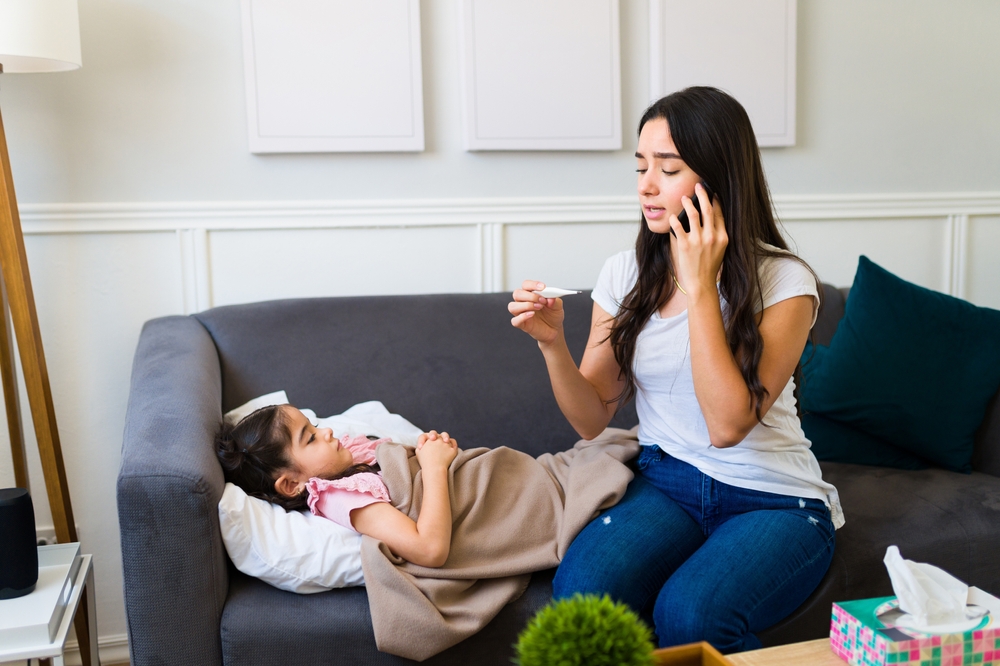 Upset young mom feeling very worried while calling a doctor on the phone because her little daughter is very sick at home

