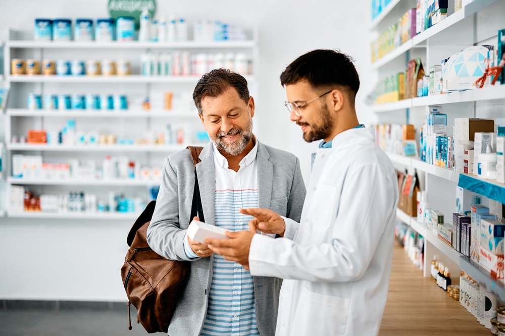 Young pharmacist talking to male customer in a drugstore. Focus is on customer.
