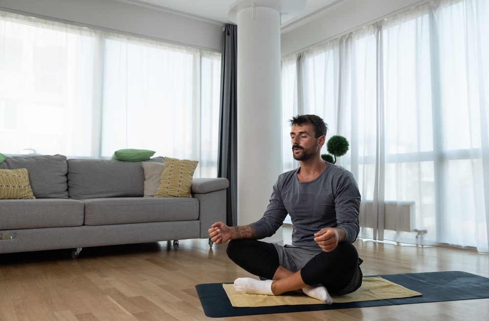 Young man cancer survivor practicing home workout yoga training, stretching muscles and breathing exercise for healthy life after long struggle with sickness and pain.
