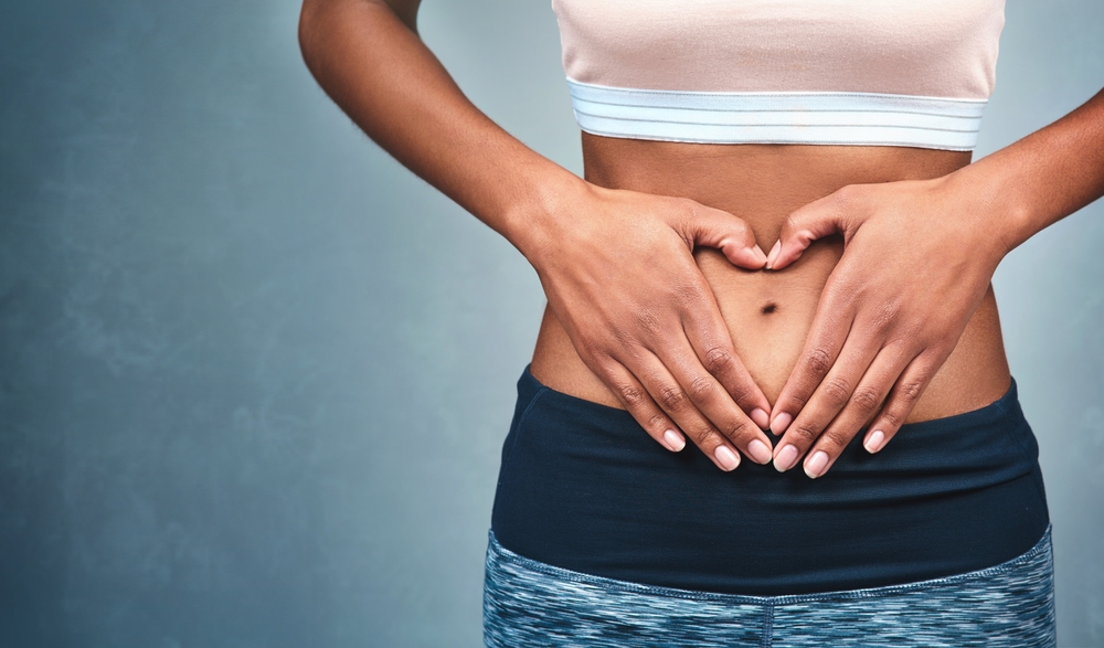 Heart, fitness and hands of a woman on a stomach isolated on a dark background in studio. Wellness, gut health and a girl with shape for love of body, weight loss and abdomen digestion on backdrop
