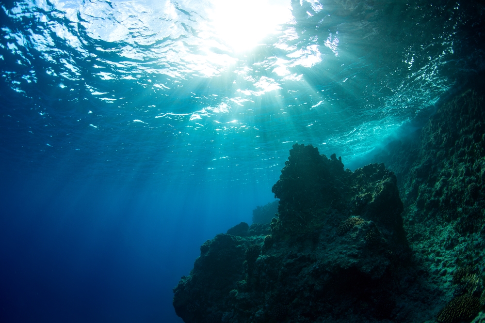 Sun burst through the clear ocean along the underwater cliff side of Guam 