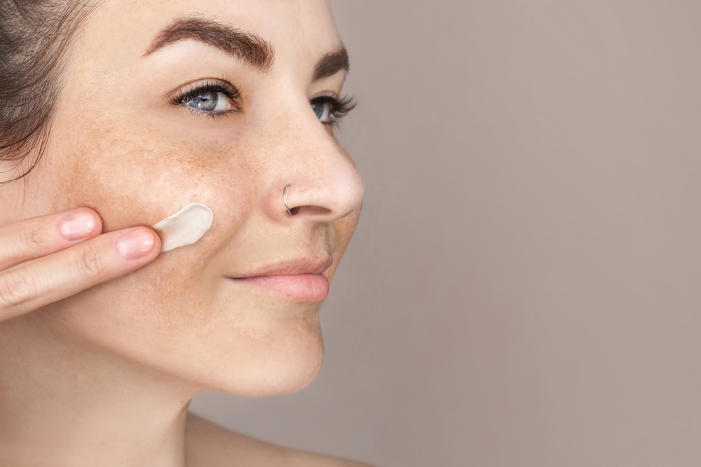 Caucasian woman's face with freckles or age spots, she smears cream on her cheek with her fingers, nice cream swatch, copy space for text close up
