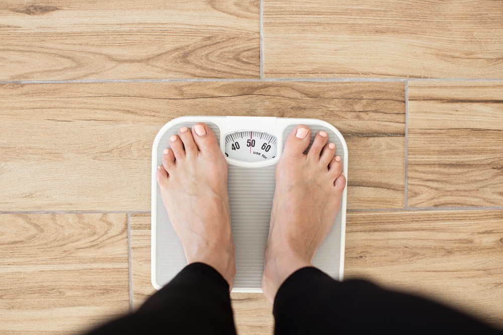 Person standing on scale measuring weight on wooden floor. Health and fitness concept focusing on weight management and wellness.

