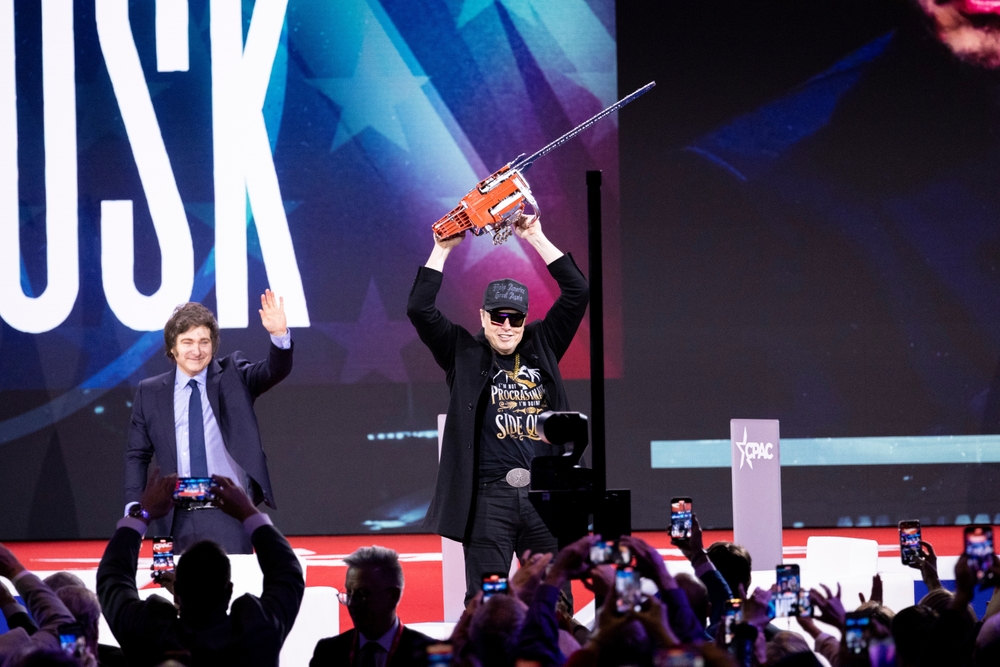 NATIONAL HARBOR, MD, USA — February 20 2025: Elon Musk wields a chainsaw, alongside President Javier Milei, and Newsmax Host Rob Schmitt on day 1 of the 2025 Conservative Political Action Conference.
