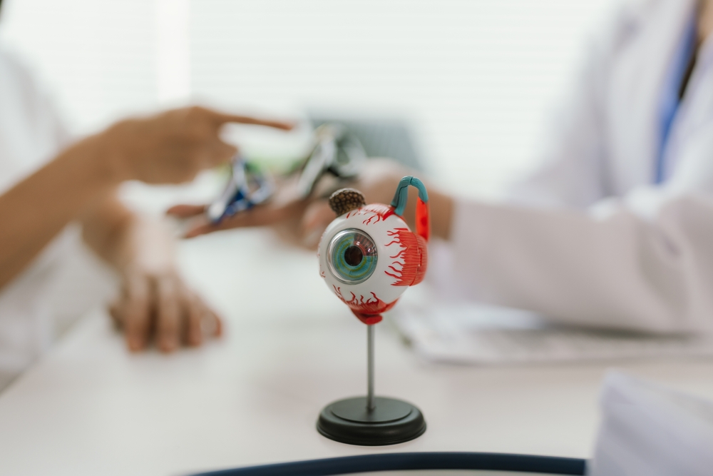 Close-up of Asian female doctor talking with elderly patient showing eyeball model and explaining eye disease in hospital
