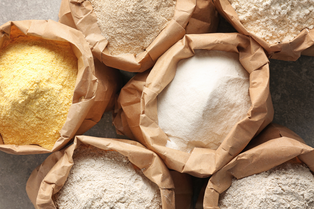 Paper bags with different types of flour on gray background, closeup