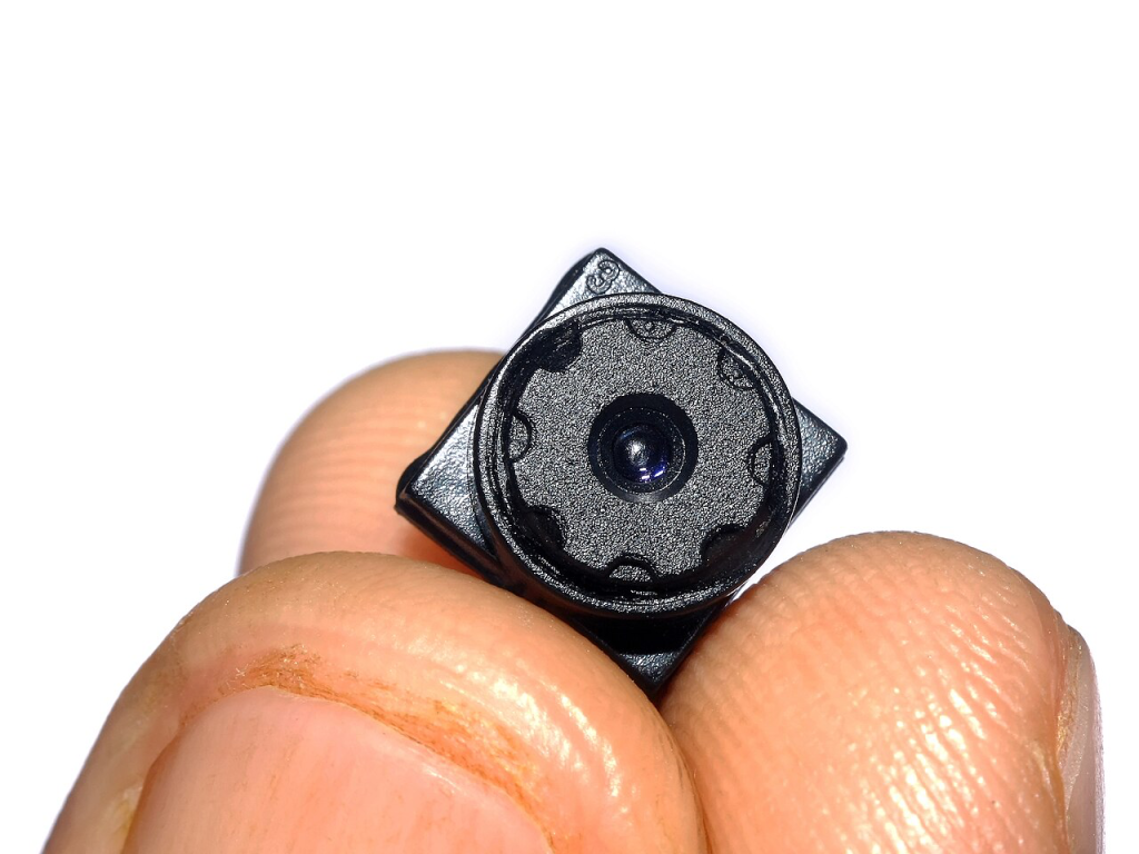 Tiny camera held between fingertips, showing actual size of hidden recording devices.