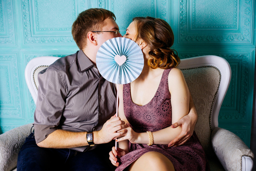 Couple playfully hides their kiss behind a decorative fan, attitudes toward kissing shifting throughout life stages.