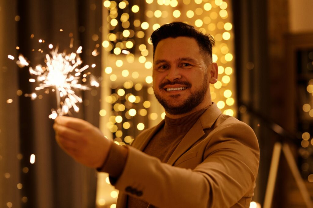 Man in Brown Coat Smiling While Holding a Burning Sparkler
