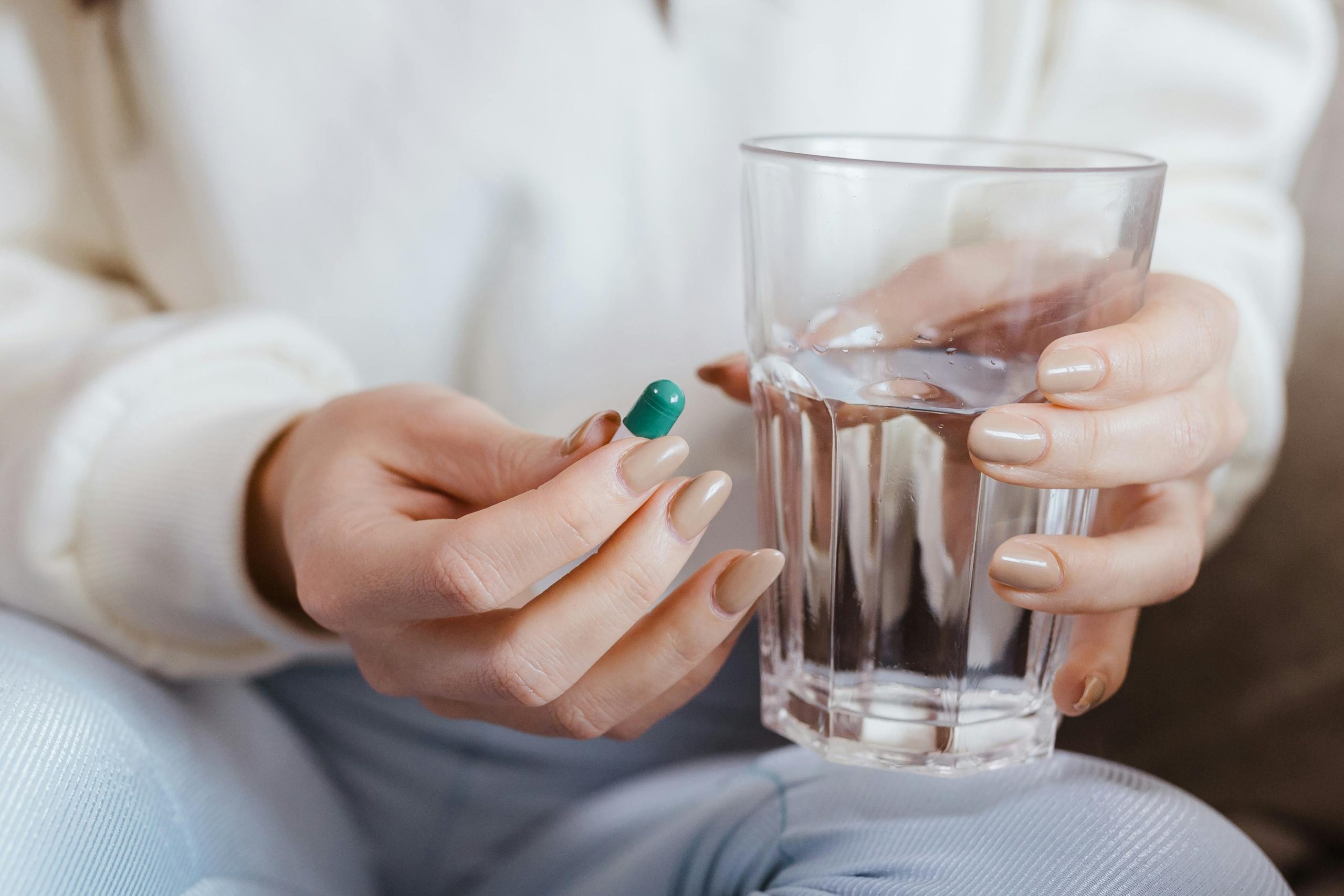 Hands holding medication capsule and water glass, demonstrating proper treatment approach.