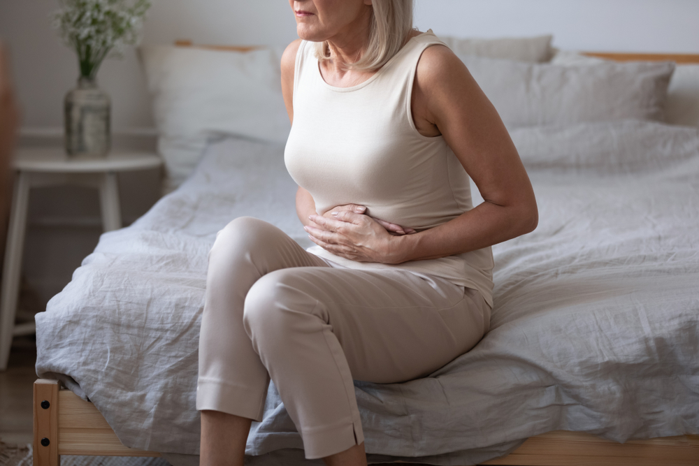 Sick upset middle aged lady hold belly suffer from abdomen ache concept, mature old adult woman feel morning pain hurt in stomach abdominal gastritis pancreatitis diarrhea problem symptom sit on bed
