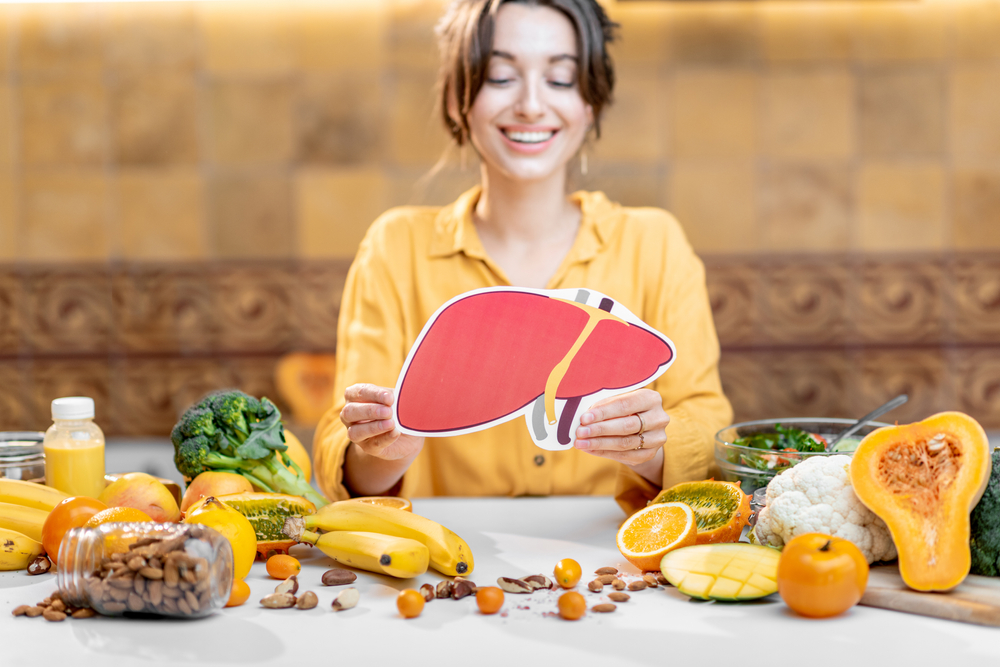 Woman holding human liver model with variety of healthy fresh food on the table. Concept of balanced nutrition for liver health
