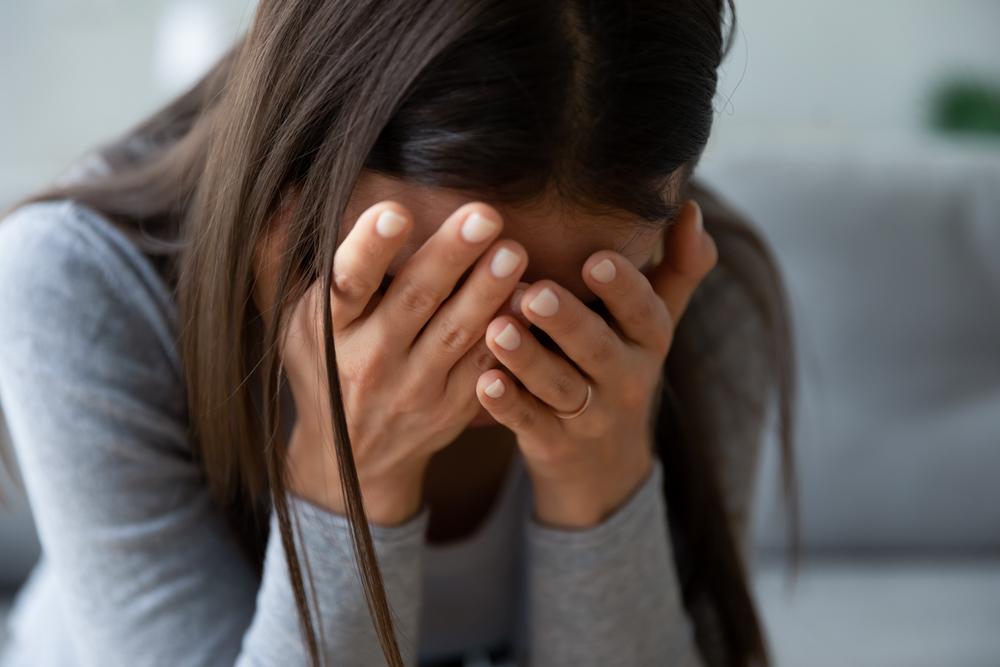 Close up unhappy young woman hiding face in hands, feeling desperate cheated hopeless alone indoors. Upset millennial girl crying, suffering from consequences of wrong decision, depression concept.