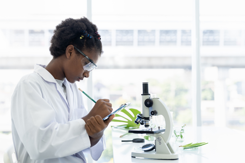 African American girl scientists learning and writing science and doing analysis for germs and bacteria with microscope in the laboratory. Science and education, researcher and discovery concept
