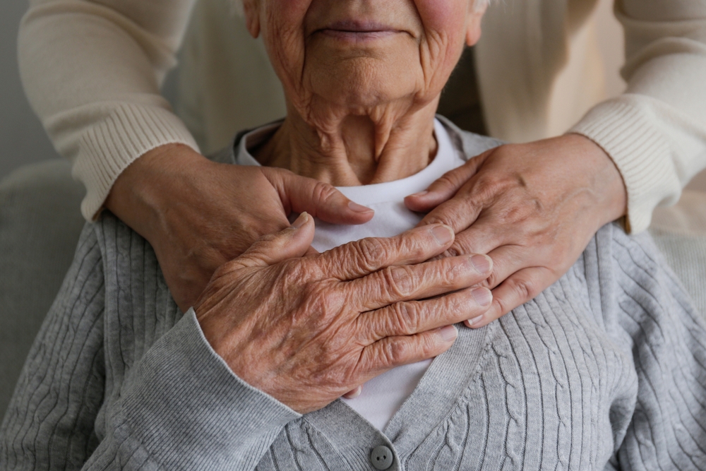 Unrecognizable female expressing care towards an elderly lady, hugging her from behind holding hands. Two adult women of different age. Family values concept. lose up, copy space, background.
