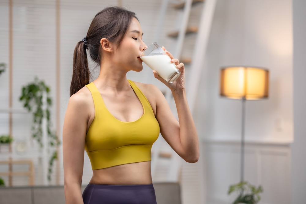 Attractive fitness asian woman finishing workout and drinking protein milk shake vitamins after training at home. Bodybuilding. Healthy lifestyle.