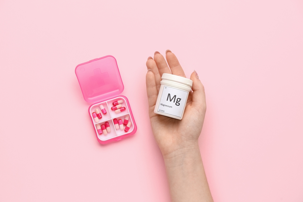 Woman holding jar of magnesium pills on pink background
